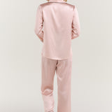 Woman lounging on bed in Jasmisilk pink silk pajama set