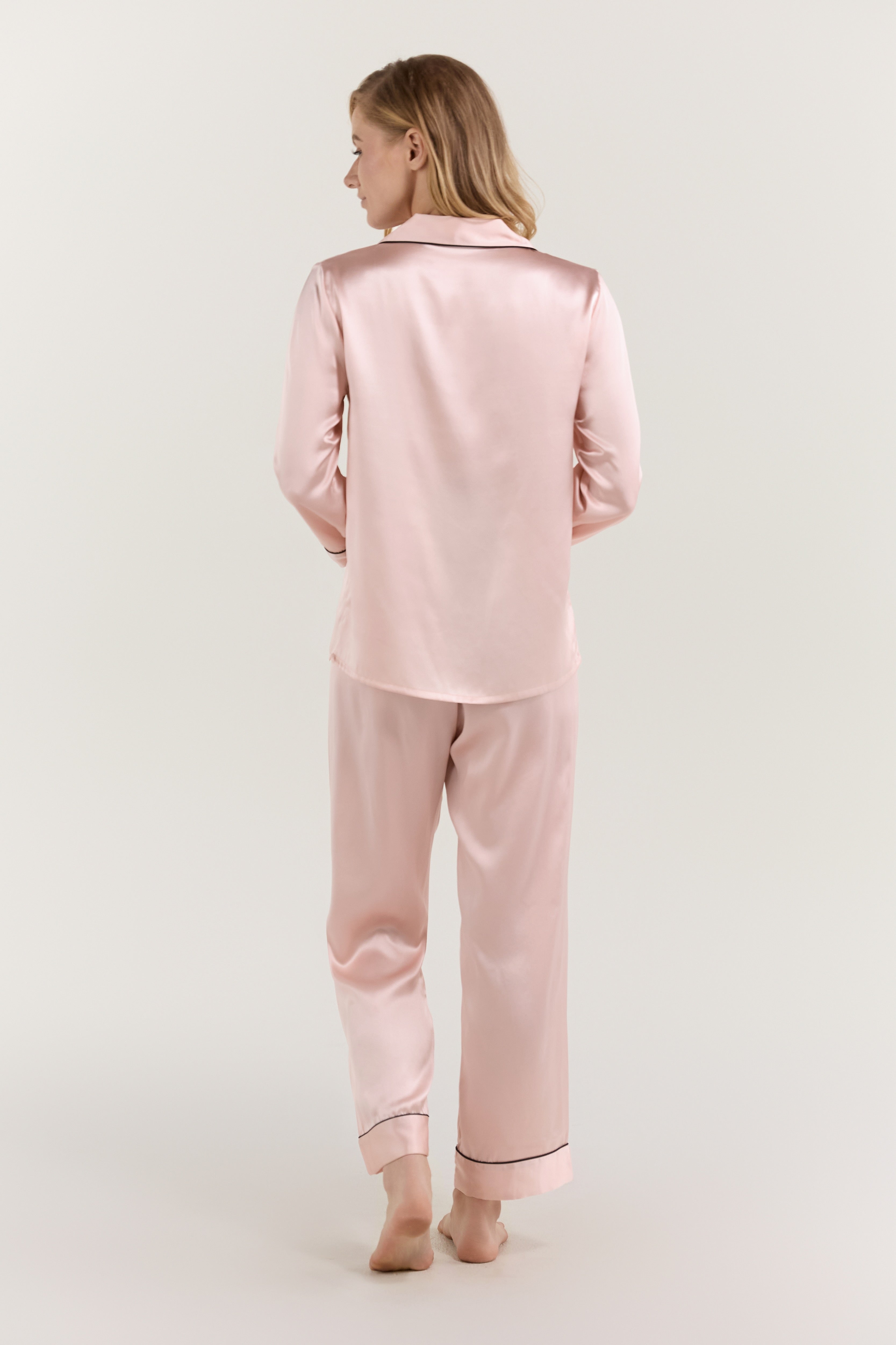 Woman lounging on bed in Jasmisilk pink silk pajama set