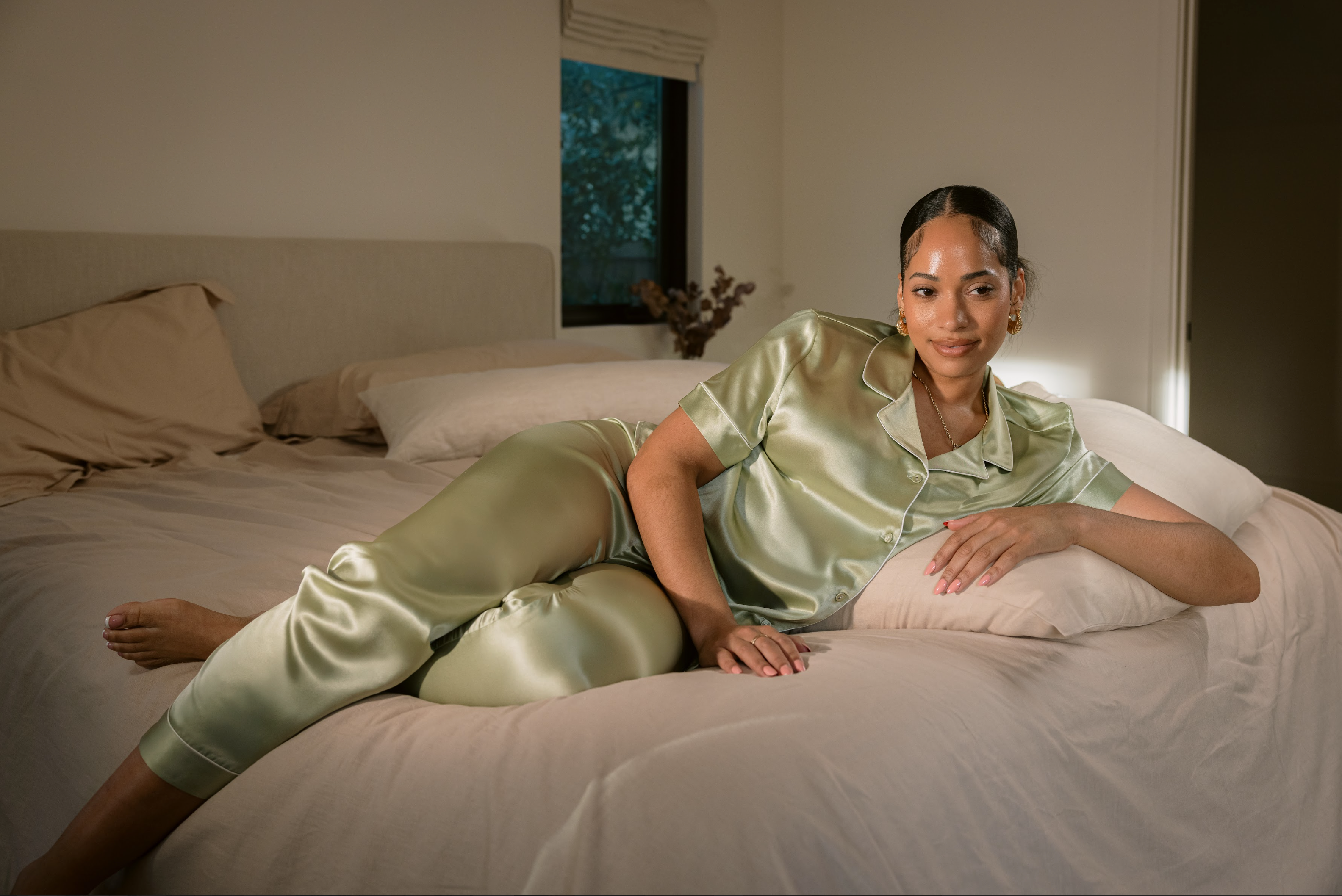 Woman in luxurious silk pajama set lounging comfortably on bed, enjoying Netflix. Perfect relaxation moment.