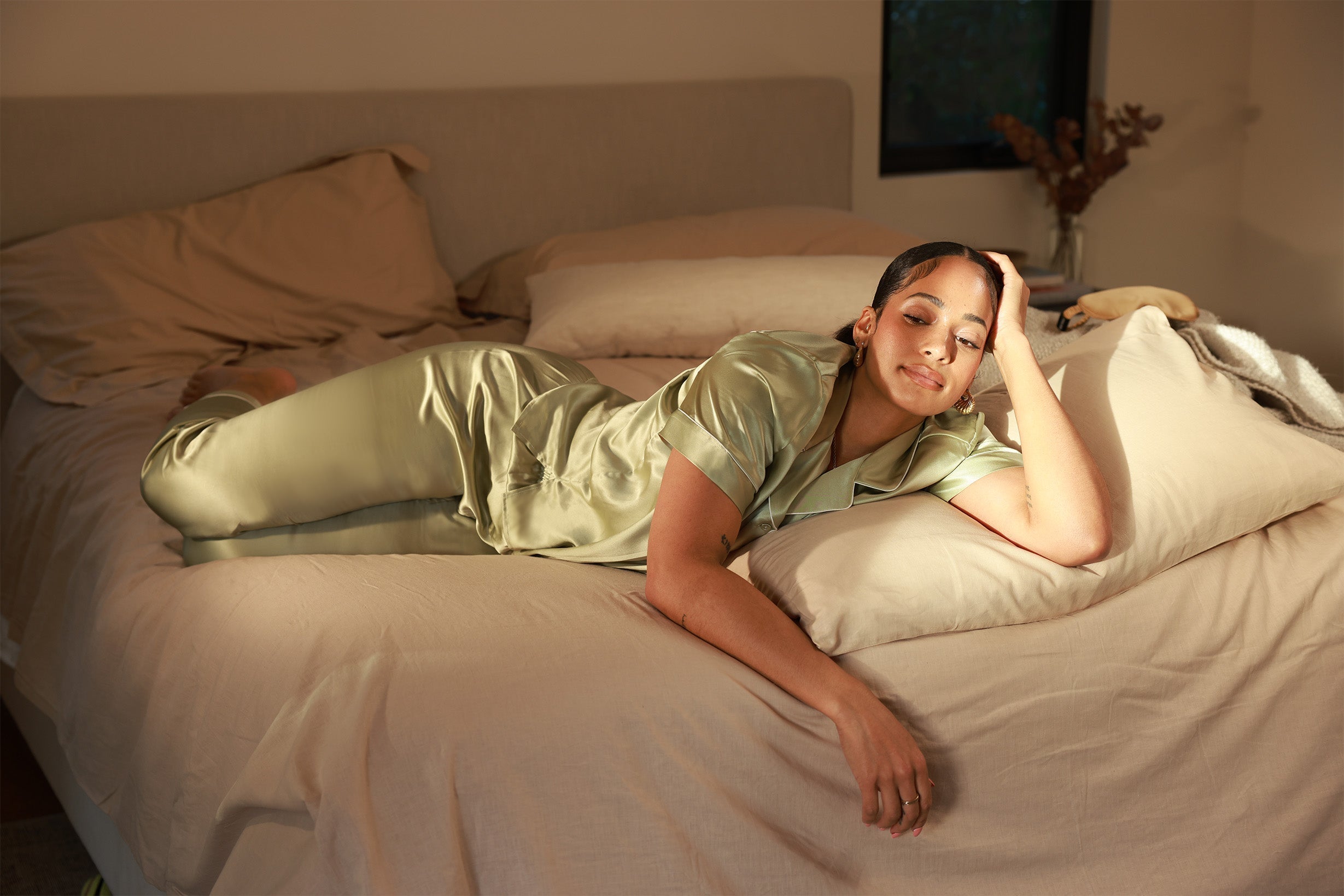 Woman lounging in silk nightwear on a sunlit bed, glowing in natural light and elegant comfort.